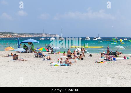 Mellieha, Malta - 30. August 2019: Menschen, die einen sonnigen Tag an einem Sandstrand mit bunten Sonnenschirmen und klarem Wasser genießen; Boote und Freizeitaktivitäten im flachen Wasser Stockfoto