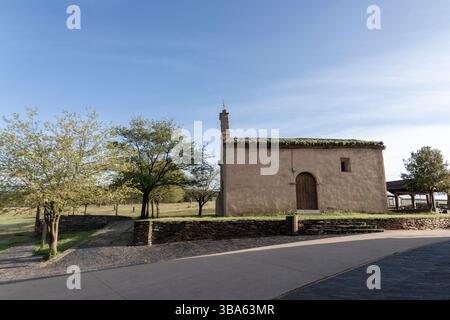 Ein kleines Gebäude mit einem grünen Dach befindet sich an einem Hügel. Das Gebäude ist von Bäumen umgeben und er ist eine Kirche. Der Himmel ist klar und die Sonne scheint Stockfoto