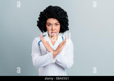 Selbstbewusste Ärztin, die eine Geste macht, die Weigerung oder Einschränkung symbolisiert, mit weißem Labormantel und Stethoskop Stockfoto