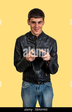 Ein Spieler lächelt und hält einen Controller, während er Videospiele spielt, trägt eine schwarze Lederjacke und eine blaue Jeans Stockfoto