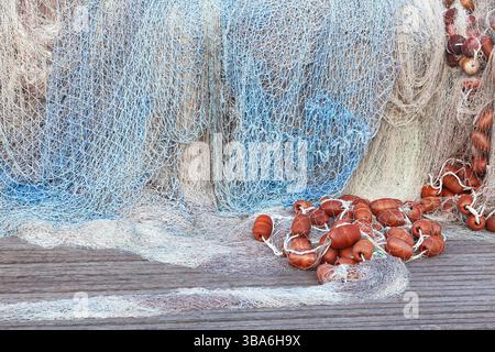 Ein großer Stapel von Fischernetzen mit Schwimmern liegt auf einem Holzsteg gesammelt. Stockfoto
