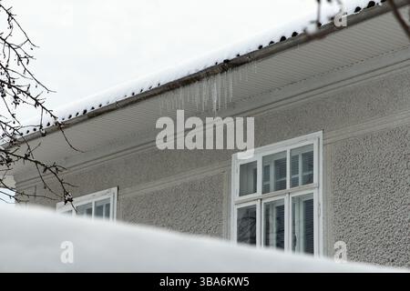 Eiszapfen hängen im Winter auf dem Schneedach eines Wohnhauses, was für die Gesundheit der Bewohner gefährlich ist Stockfoto