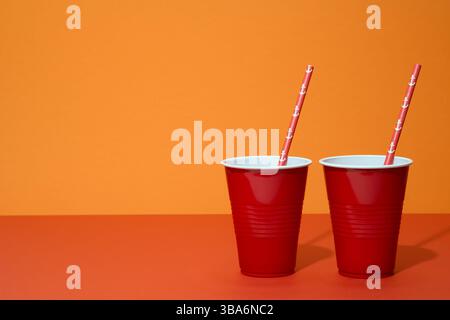 Rote Plastikgläser mit roten Strohhalmen auf orangem Hintergrund. Stockfoto