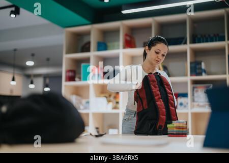 Junge Frau, die Rucksack in modernen Büroräumen organisiert Stockfoto