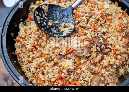 Blick von oben auf fertige orientalische Pilaw in einem schwarzen Kessel auf einem Tisch im Freien Stockfoto