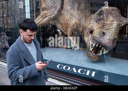 Besucher auf der Regent Street kommen am 24. März 2025 in London, Großbritannien, an einem großformatigen Modell eines Tyrannosaurus Rex im Schaufenster von Coach vorbei. Die Regent Street ist ein bedeutendes Einkaufszentrum im West End der Hauptstadt und ist bekannt für seine Flaggschiff-Einzelhandelsgeschäfte, von denen die meisten Mode-, High Street- und High-End-Bekleidungsgeschäfte sind. Stockfoto