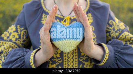 Ukrainische Frau in einem Hemd mit gelbem Muster hält ein gestricktes ukrainisches Herz in den Händen. Unabhängigkeitstag, Vyshyvanka-Tag. Ukrainer AS Stockfoto