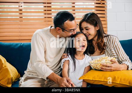 Eine glückliche Familie voller Freude schaut fern, während sie auf einem modernen Sofa zu Hause Popcorn isst Stockfoto