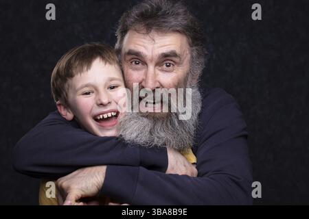 Porträt eines glücklichen Großvaters mit Bart und Enkel auf schwarzem Hintergrund Stockfoto