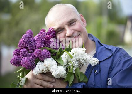 Älterer Mann mit einem Blumenstrauß brutaler grauhaariger Mann mit einem schönen Flieder Stockfoto