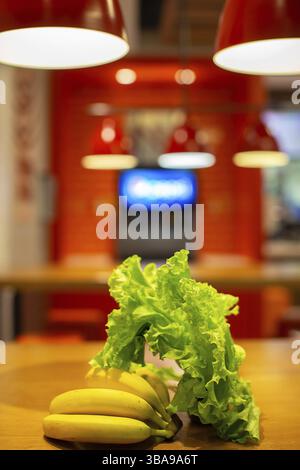 Gemüse und Obst vor dem Hintergrund einer verschwommenen Küche. Bananen und Salat auf dem Küchentisch Stockfoto