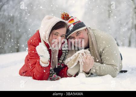 Ein wunderschönes Paar mittleren Alters schaut vor dem Hintergrund einer Winterlandschaft in die Kamera. Mann und Frau im Winter Stockfoto