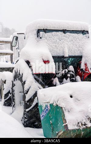 Ein schneebeladener Traktor sitzt im Leerlauf in einer Dorfgasse, seine Räder und das Fahrerhaus sind fast unter Peiseys dicken Wintermantel vergraben. Stockfoto