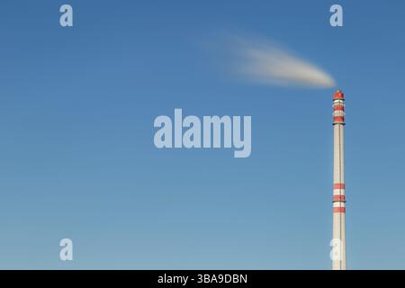 Industrieller Schornstein im Wind. Schmutziger Rauch aus rotem und weißem Fabrikschornstein am blauen Himmel. Langzeitbelichtung, Platz für Text, Prag, Tschechische Republik, Euro Stockfoto
