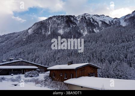 Ein schneebedecktes Chalet befindet sich unter einem dunklen Waldrücken unter stimmungsvollem Himmel und fängt die alpine Stille des Winters in Peisey ein. Stockfoto