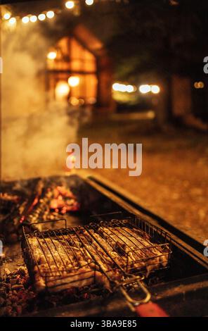 Nahaufnahme eines abendlichen Barbecue im Hinterhof des Hauses. Köstliches saftiges, duftendes Fleisch auf dem Grill und brennende Holzkohle. Leckeres Essen im Freien. Tr Stockfoto