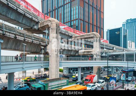 Bangkok, Thailand - 19. März 2025: Hochbahngleise und Fußgängerweg über der belebten Straße mit Verkehr und Hochhäusern in Bangkok Stockfoto
