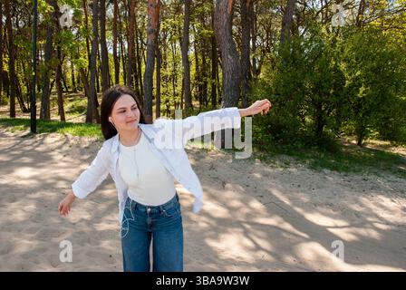 Junge Erwachsene weiße Erwachsene an einem Sandstrand mit weißem Oberteil und blauer Jeans, die freudig einen sonnigen Tag inmitten üppiger grüner Bäume genießen. Digitaler Nomade Stockfoto