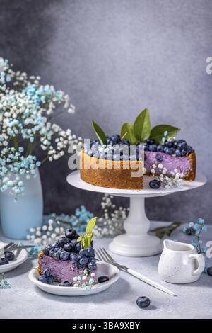 Süßer cremiger Blaubeer-Käsekuchen mit frischen Blaubeeren und Schlagsahne mit geschnittenem Stück auf hellem Hintergrund, Beerenkuchen. Französische Küche Stockfoto