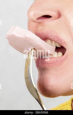 Eine Frau, deren Gesicht nicht sichtbar ist, hält eine Gabel mit Wurst im Mund Stockfoto