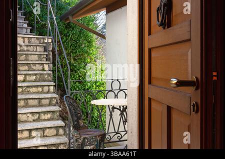 Offene Eingangstür eines Apartments führt zu einem kleinen Balkon und zu einer Treppe im Garten Stockfoto