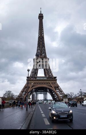 Paris, Frankreich - 4. Dezember 2021: Autos fahren auf der Straße unter dem Eiffelturm an einem dunklen, bewölkten, regnerischen Herbsttag in Paris, Frankreich. Stockfoto