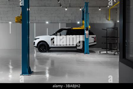 Weißer Range Rover in der Autowerkstatt. Seitenansicht des Luxus-SUV-Wagens in einer leeren Autowerkstatt für Wartungsarbeiten. Stockfoto