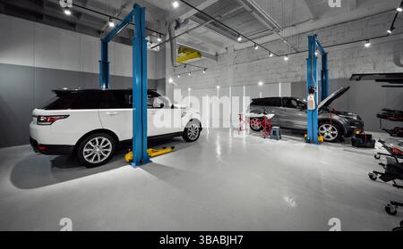 Autowerkstatt mit zwei SUVs. Seitenansicht von zwei Luxusautos in leerer Autowerkstatt, technische Wartung. Stockfoto