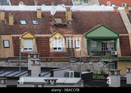 Nahaufnahme eines städtischen Gebäudes mit rot gekachelten Dächern, farbenfrohen Fenstern und Balkonen, die eine Mischung aus Architektur und Stadtleben einfangen. Stockfoto