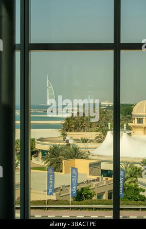 Ein Blick durch ein großes Glasfenster zeigt eine Küstenszene mit Palmen, Sandstrand und ikonischer Architektur im Hintergrund, einschließlich einer ta Stockfoto