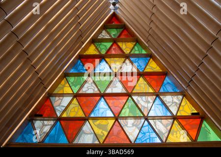 Ein farbenfrohes Buntglasfenster mit dreieckigen Mustern in einer modernen architektonischen Umgebung. Das Fenster ist beleuchtet und zeigt leuchtende Farben Stockfoto