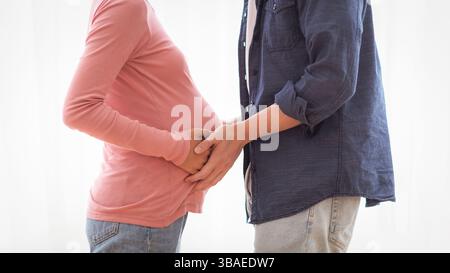 Glücklicher koreanischer Ehemann berührt schwangeren Frau Bauch zu Hause stehend Stockfoto