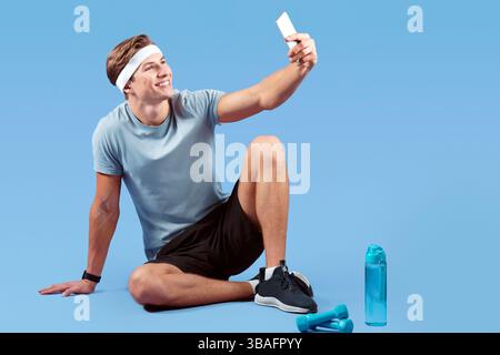 In voller Länge Porträt von positiven jungen Kerl unter Selfie mit Smartphone nach dem Training auf violettem Studiohintergrund Stockfoto