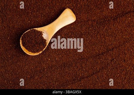 Gemahlener Kaffee und ein kleiner Holzlöffel, eine große Anzahl gerösteter gemahlener Kaffeebohnen in Pulver und ein Holzlöffel, Nahaufnahme, Blick von oben Stockfoto