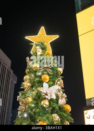 Weihnachtsbaum mit goldenem Stern oben, alle beleuchtet in der Stadt. Stockfoto