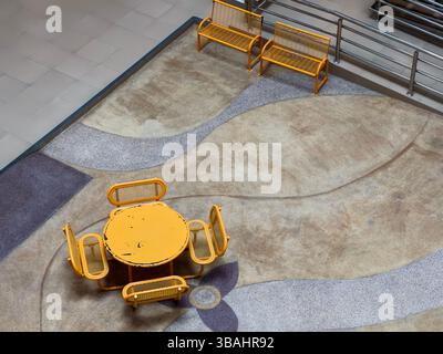 Blick von oben auf einen stilvollen Innensitzbereich mit einem runden Tisch in leuchtendem Gelb, passenden Stühlen und eleganten gelben Bänken. Stockfoto