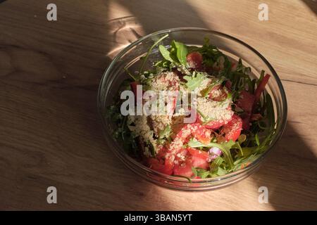 Gesunder Salat mit Rucola, Tomaten und Paprika, garniert mit Hefeflocken, auf einem rustikalen Holztisch. Nahrhaft und Stockfoto