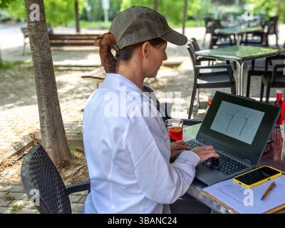 Ingenieurin, die Windturbinen auf Laptop in einem Café im Freien entwirft Stockfoto