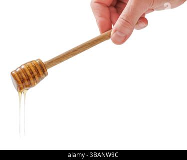 Nahaufnahme einer Hand, die einen handgefertigten Löffel aus Holz mit goldenem Honig hält, der auf weißem Hintergrund tropft, horizontale Ansicht, reales Foto, nicht KI-generiert Stockfoto