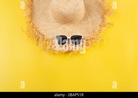 Urlaubsreiseplanung einfaches Thema von Strohhut und Sonnenbrille auf einheitlichem gelbem Hintergrund flach gelegt mit Kopierraum Stockfoto