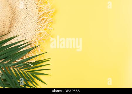 Urlaubsreiseplanung einfaches Thema von Strohhut und Palmblättern auf einheitlichem gelbem Hintergrund flach mit Kopierraum Stockfoto