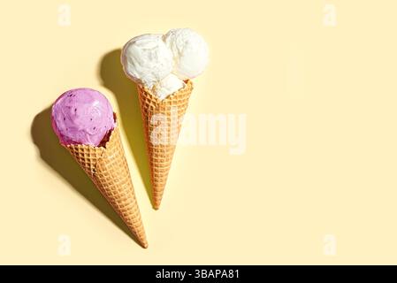 Zwei Eiswaffelkegel mit Vanille- und Heidelbeeraromen auf gelbem Pastellhintergrund, Draufsicht, Kopierraum. Kreatives, trendiges Eis-Layout, Sommer d Stockfoto