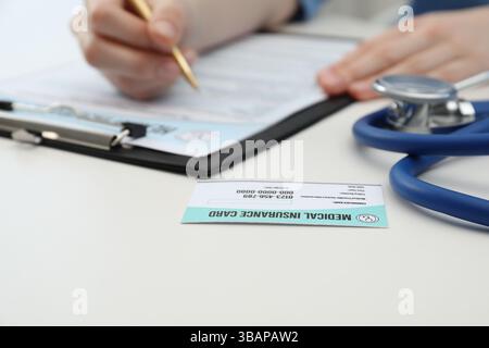 Doktor mit Stift ausfüllen Policenformular am weißen Tisch, Fokus auf Krankenversicherungskarte Stockfoto