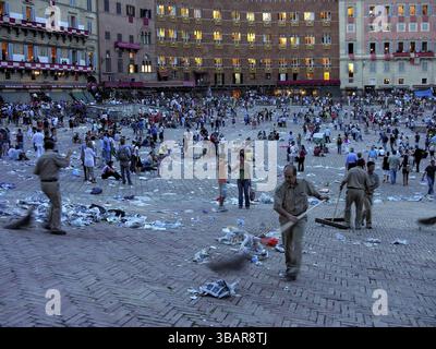 IL Palio di Siena, historisches Pferderennen, Arbeiter, die den Platz nach dem Rennen von Müll reinigen, Palazzo Sansedoni mit Hintergrundbeleuchtung, blaue Stunde, Piazza del Ca Stockfoto