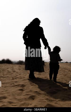 Die Mutter hält die Kinderhand, die tagsüber in der Wüste spaziert. Das hintergrundbeleuchtete Foto wurde in rajasthan, Indien, aufgenommen. Stockfoto