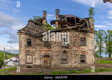 Altes verlassenes Gebäude, das mit beschädigtem Dach und gebrochenen Fenstern auseinanderfällt, zeigt den Lauf der Zeit und die Kraft der Natur Stockfoto