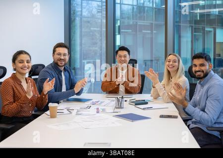 Eine vielfältige Gruppe von Fachleuten feiert einen Erfolg während eines Meetings und klatscht mit einem Lächeln um einen Tisch. Stockfoto