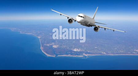 Weißes Passagierflugzeug fliegt an einem sonnigen Tag über der wunderschönen Küste, aus der Luft Stockfoto