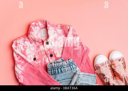 Stylisches Outfit für Kinder Bekleidung aus Denim. Pinke Denim-Jacke und Jeans mit glänzenden Sneakern auf rosa Hintergrund. Halten Sie Ausschau nach Frühling oder Sommer Stockfoto