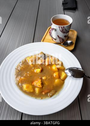 Dichte Kartoffelsuppe mit Kartoffeln und Waldpilzen und Spiegelei auf Teller mit einer Tasse Tee. Diese Suppe ist sauer, manchmal wird Dill hinzugefügt Stockfoto